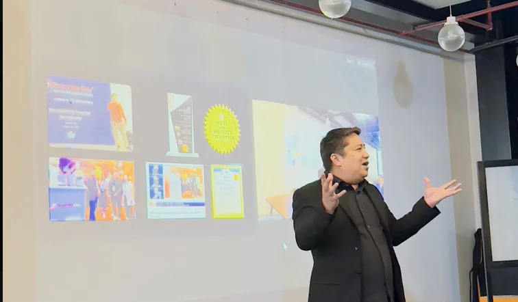 Jas Barinaga presenting to a small group in a training room, with slides projected behind him.