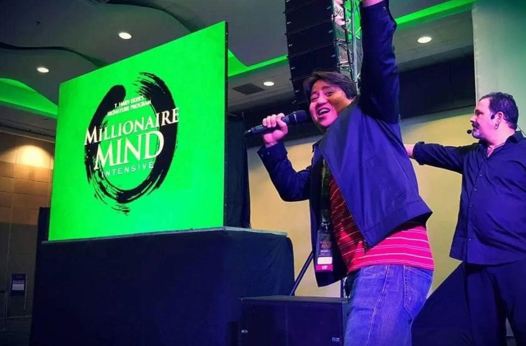 Jas Barinaga on stage with a microphone at the Millionaire Mind Intensive.